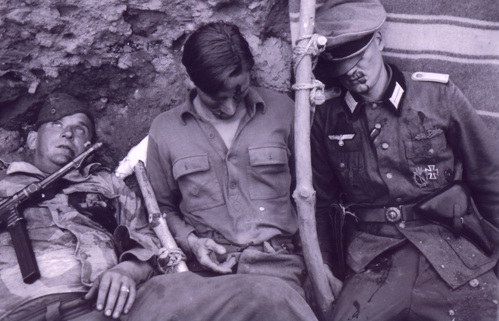 Wounded soldiers slumped together — an Italian partisan, an American GI, and a German officer