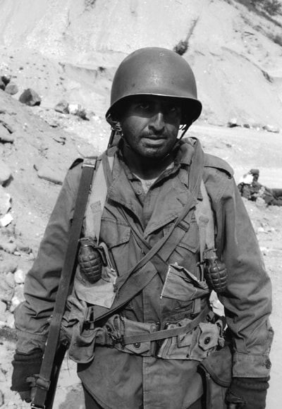 American soldier in full combat gear standing against a rocky hillside