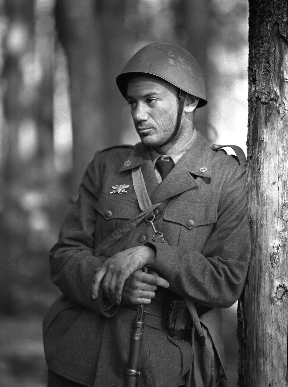 Italian soldier leaning against a tree in the forest, holding his rifle